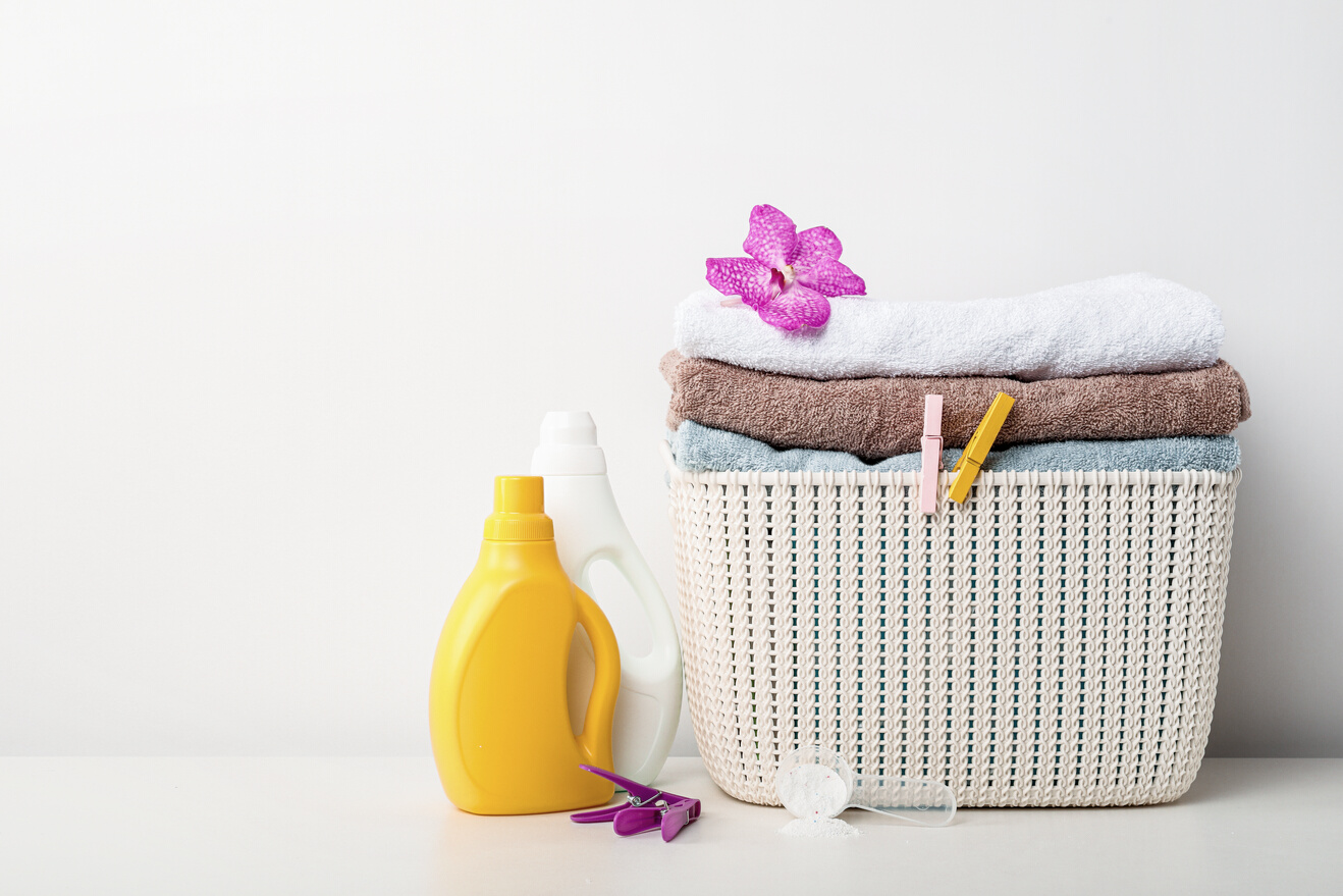 Laundry basket with towels, detergents, soap and bamboo balls on white background